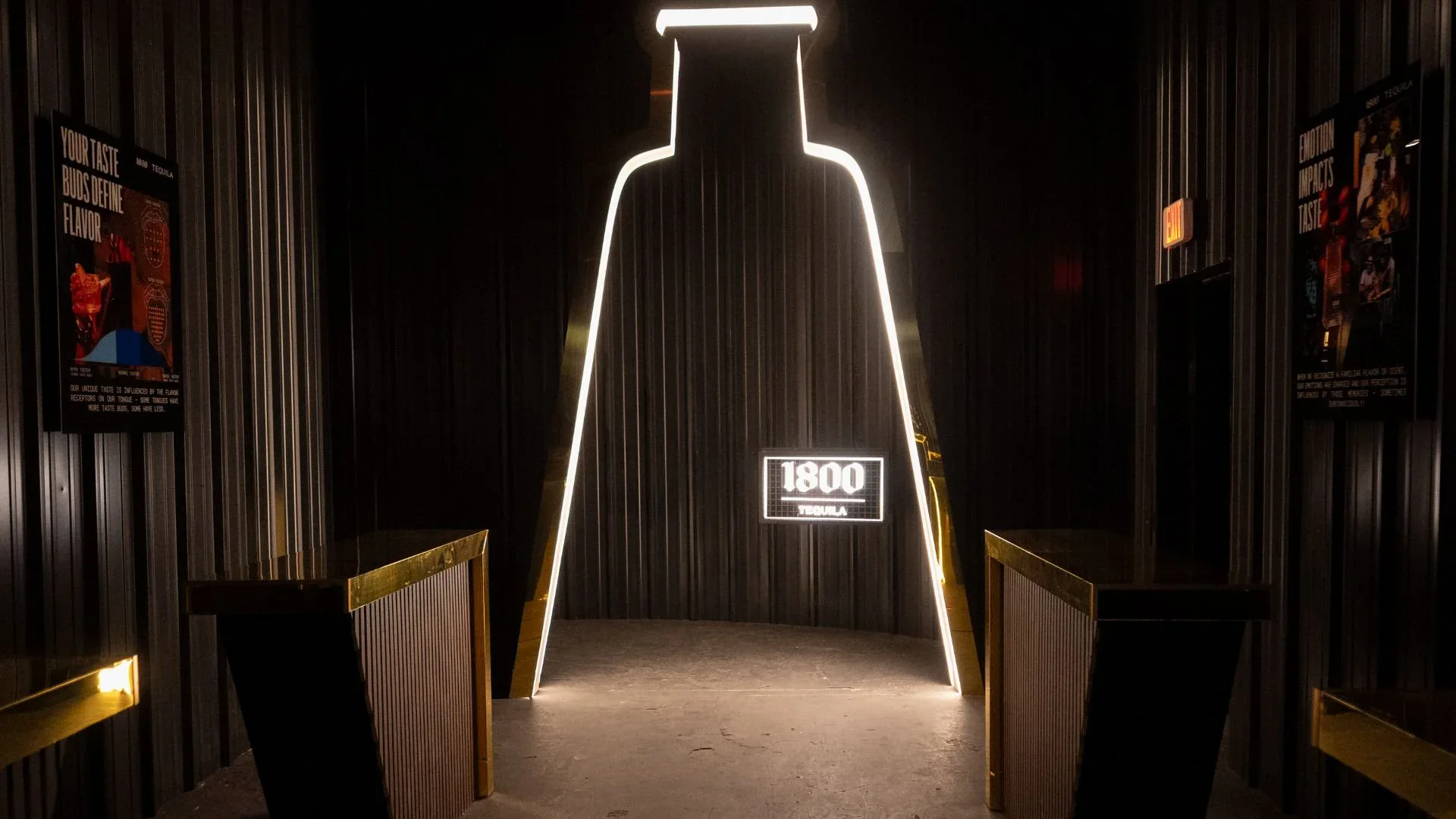 A bottle-shaped neon doorway glowing in a black corrugated corridor