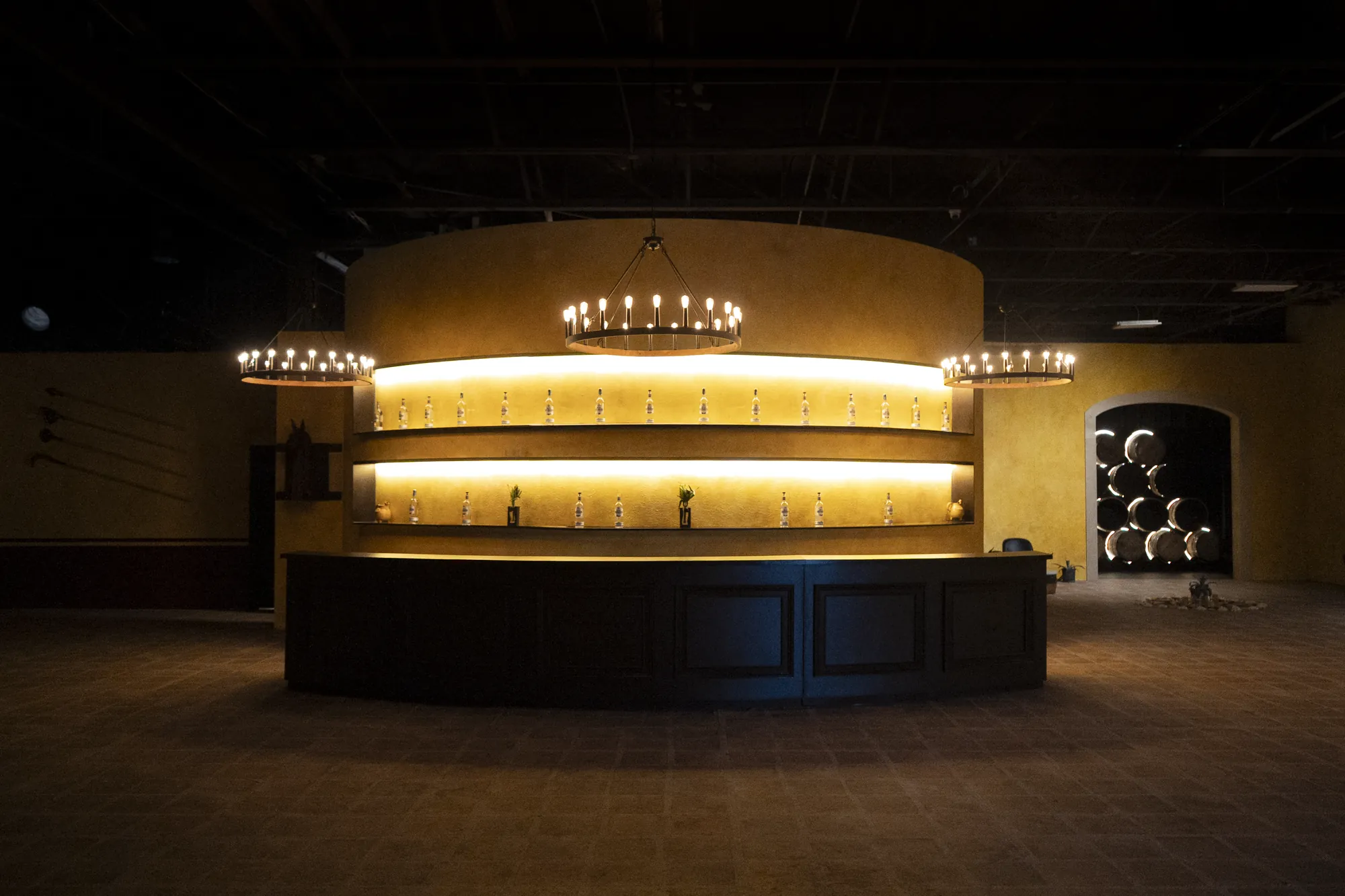 The curved, lit bar of La Rojeña beneath iron ring chandeliers, with open floor in front for a reception